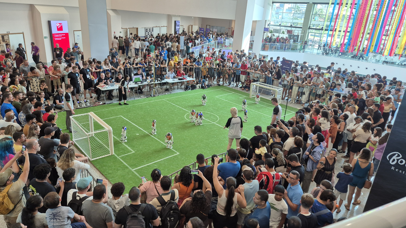 Zahlreiche Zuschauende stehen dicht gedrängt um ein Spielfeld auf dem Robotor Fußball spielen