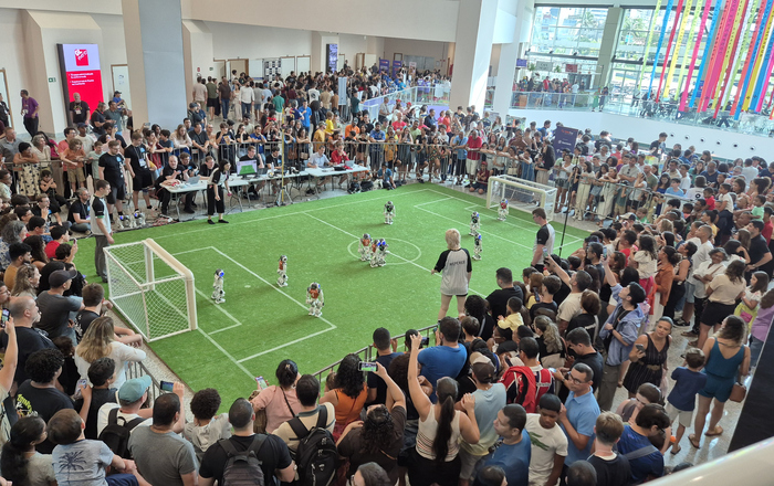 Zahlreiche Zuschauende stehen dicht gedrängt um ein Spielfeld auf dem Robotor Fußball spielen