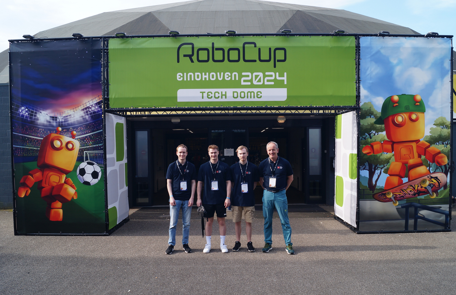 Vier Männer stehen vor dem Eingangsportal zum RoboCup 2024 
