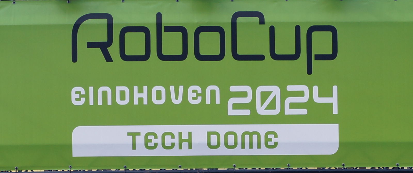 Vier Männer stehen vor dem Eingangsportal zum RoboCup 2024 