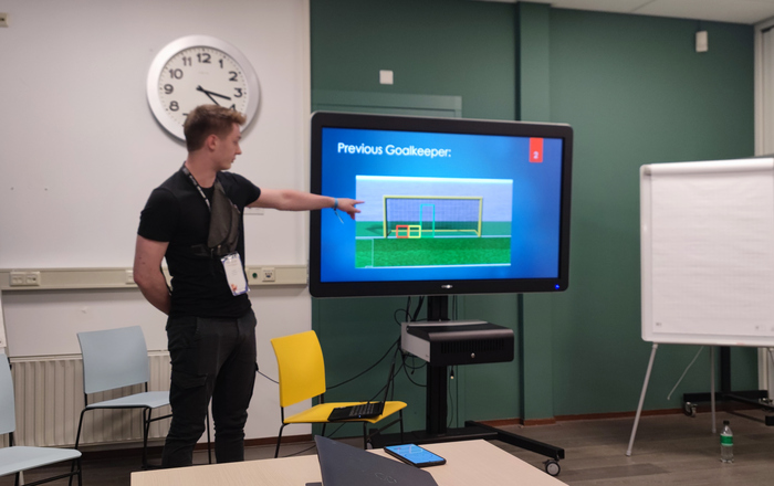 Ein junger Mann steht links neben einem Bildschirm und erläutert Funktion des Torhüters darauf